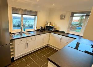 a kitchen with white cabinets and a sink and two windows at Oaktree Cottage, overlooking Loch Fyne in Cairndow