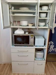 a white cabinet with a microwave and dishes in it at つるふく in Misaki