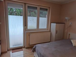 a bedroom with two windows and a bed and a refrigerator at Benett Apartman in Győr