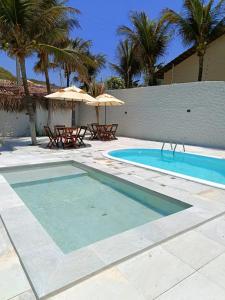 a swimming pool with two tables and an umbrella at Vila Refúgio in Aracati