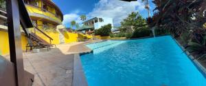 a swimming pool next to a yellow building at Suíte Atobás in Arraial do Cabo