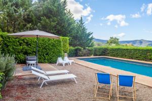 a patio with chairs and an umbrella and a pool at Villa des Amandes in Bédarieux
