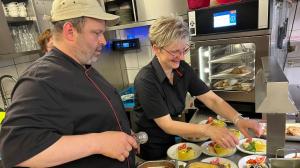 Ein Mann und eine Frau bereiten Essen in einer Küche zu. in der Unterkunft Hotel Sonnekalb in Naumburg