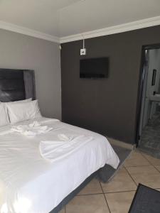 a bedroom with a white bed with a tv on the wall at The Good Samaritan 4 in eMalahleni