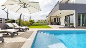 a pool with chairs and an umbrella next to a house at Villa Kali in Krnica