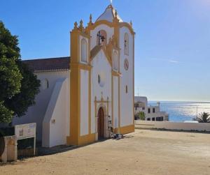a church with a clock tower in front of the ocean at Casa Prainha da Luz in Luz