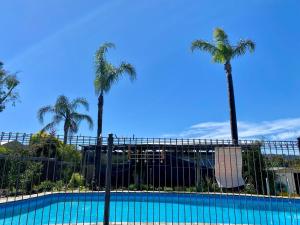a fence with palm trees and a swimming pool at Hillside Retreat with Pool in Flagstaff Hill