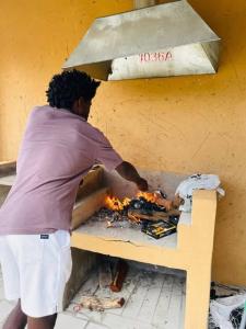 a man cooking food in an outdoor oven at Cozy Road Lodge in Sihangwane