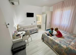2 bambini seduti sui letti in una camera d'albergo di Hotel Belvedere a Sottomarina
