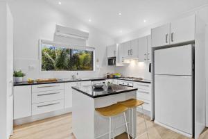 a kitchen with white cabinets and a white refrigerator at Mollymook Den Coastal Retreat - Walk to Beach & Town in Mollymook