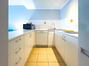 a small kitchen with white cabinets and a microwave at Mango Reef House - Airlie Beach in Airlie Beach