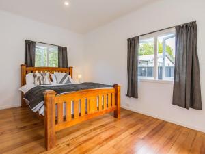 a bedroom with a wooden bed and two windows at Aroha Cottage in Ohakune