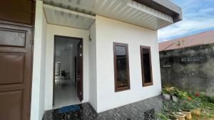 a white house with a door and a balcony at Denggan KNO Guest House in Tanjungmorawa