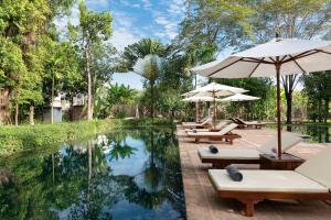 una piscina con sedie a sdraio e ombrelloni accanto al resort di The Elephant a Siem Reap