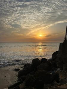 a sunset over the ocean with rocks on the beach at Chambre avec salle de bain privative proche de la plage et de Saly in Mbour
