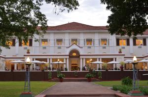 a large white building with tables and umbrellas at The Victoria Falls Hotel in Victoria Falls