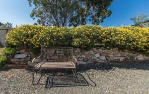a bench sitting in front of a stone wall with flowers at Barossa Valley’s Captain Rodda’s Cottage in Angaston