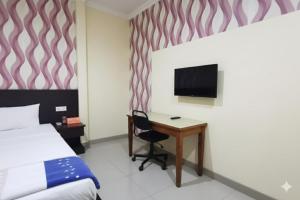 a bedroom with a desk and a bed and a tv at OYO 95059 Ikon Guesthouse in Sengata