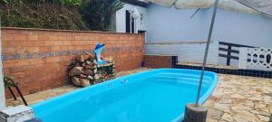 a blue swimming pool with an umbrella next to a house at chalé casa na mata céu Iluminado in Guararema +18 photos