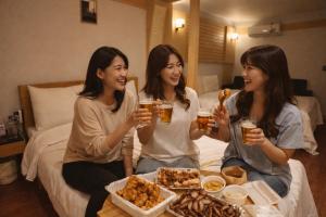 three women sitting on a bed holding glasses of beer at 평촌코아 in Mabun-ni