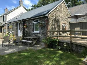 a stone cottage with a table and a wooden deck at Sgubor Delyn Aberystwyth in Llanrhystyd