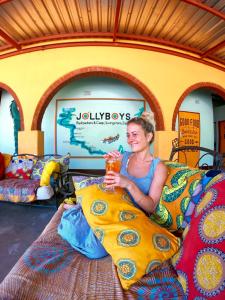a woman sitting on a bed holding a drink at Jollyboys Backpackers and Camp in Livingstone