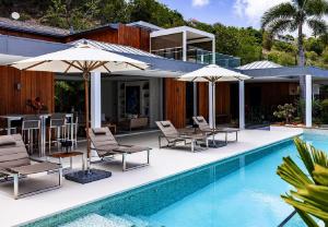 a pool with chairs and umbrellas next to a house at Tropical heaven in Les Trois-Îlets
