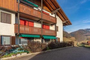 a building with balconies and red windows with mountains in the background at Trilo Ciasa Brìma in Carano