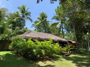 a hut with a straw roof and some trees and grass at Bangalô 12 in Porto Seguro