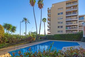 a swimming pool in front of a building with palm trees at Vue mer port de garavan in Menton