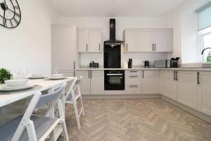 a kitchen with white cabinets and a table with chairs at Modern 2 Bedroom Cottage Flat in Stenhousemuir