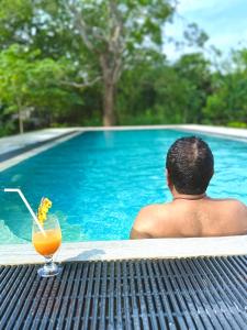 a man sitting on a table next to a pool with a drink at Turtle Pond Wilpattu in Wilpattu