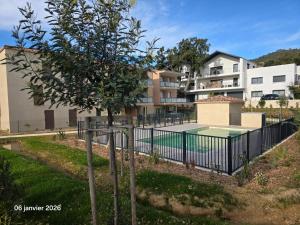 a fence with a tennis court in front of a building at Spacieux appartement dans résidence avec piscine in Bormes-les-Mimosas