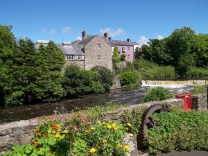 a house and a river with a bridge and flowers at Kiln Wing, Old Corn Mill in Bushmills