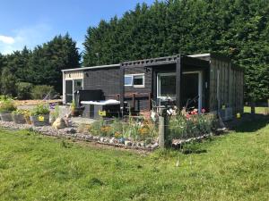 a black tiny house in a yard with flowers at Brookside Country Escape 40 minutes to CHC Airport in Leeston
