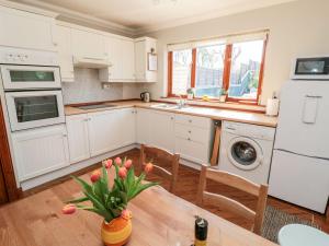a kitchen with white cabinets and a table with a vase of flowers at Cygnet Cottage in Berwick-Upon-Tweed