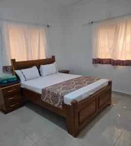 a bedroom with a bed and a nightstand and two windows at JEK Villa in Brufut