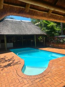 a large blue swimming pool with a thatch roof at Rosies on Robin - Pool, Braai & Mountain Views in Rustenburg