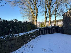 a snow covered yard with a stone fence and trees at The Bronte Moor Retreat - 3 Bed, Pet Friendly Cottage - Stunning Views - Hot Tub in Heptonstall