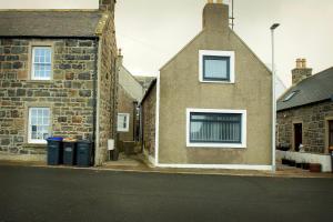 a brick house with two windows and two trash cans at Coorie-In Cottage in Whitehills