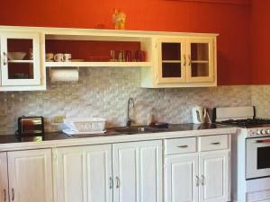 a kitchen with white cabinets and a red wall at Tropical Tabago in Carnbee Village
