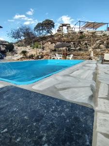 a swimming pool with blue water in front of a house at Recanto das Pedras hospedagem - Suíte 3 in São Thomé das Letras