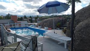 a swimming pool with an umbrella and a bench next to it at CABAÑAS BALCON DE PEHUMAYEN in Villa Carlos Paz