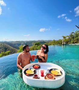 a man and woman sitting in the water with a table in the ocean at Green Coco Suite by AGATA in Nusa Penida