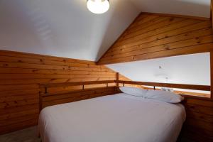 a bedroom with a white bed with wooden walls at Smoke Lake Hot Springs Lodge & Camp in Rotorua