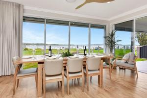 a dining room with a table and chairs and large windows at Tilligerry Beach Retreat in Taylors Beach