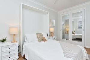 a white bedroom with a white bed and a mirror at Tilligerry Beach Retreat in Taylors Beach