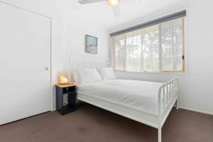 a white bedroom with a bed and a window at Casa LuCe by Experience Jervis Bay in Erowal Bay