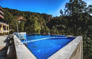 a blue swimming pool with a mountain in the background at Vedikant Pine Tree Resort in Chail