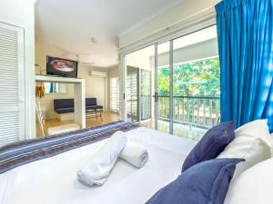 a bedroom with a bed with blue curtains and a large window at Mango Eden Villa in Airlie Beach